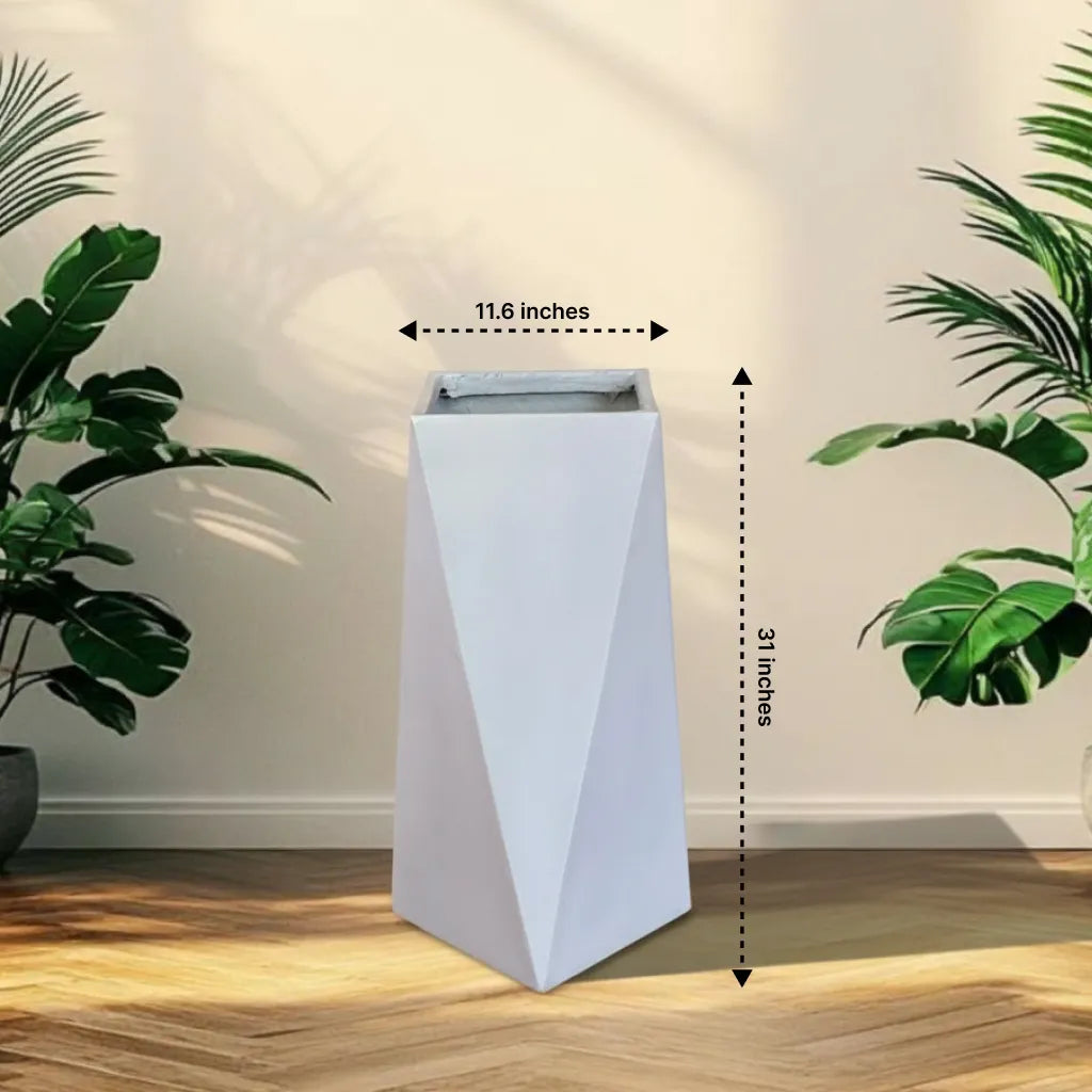 White geometric planter with dimensions labeled, placed on a wooden floor with plants around.